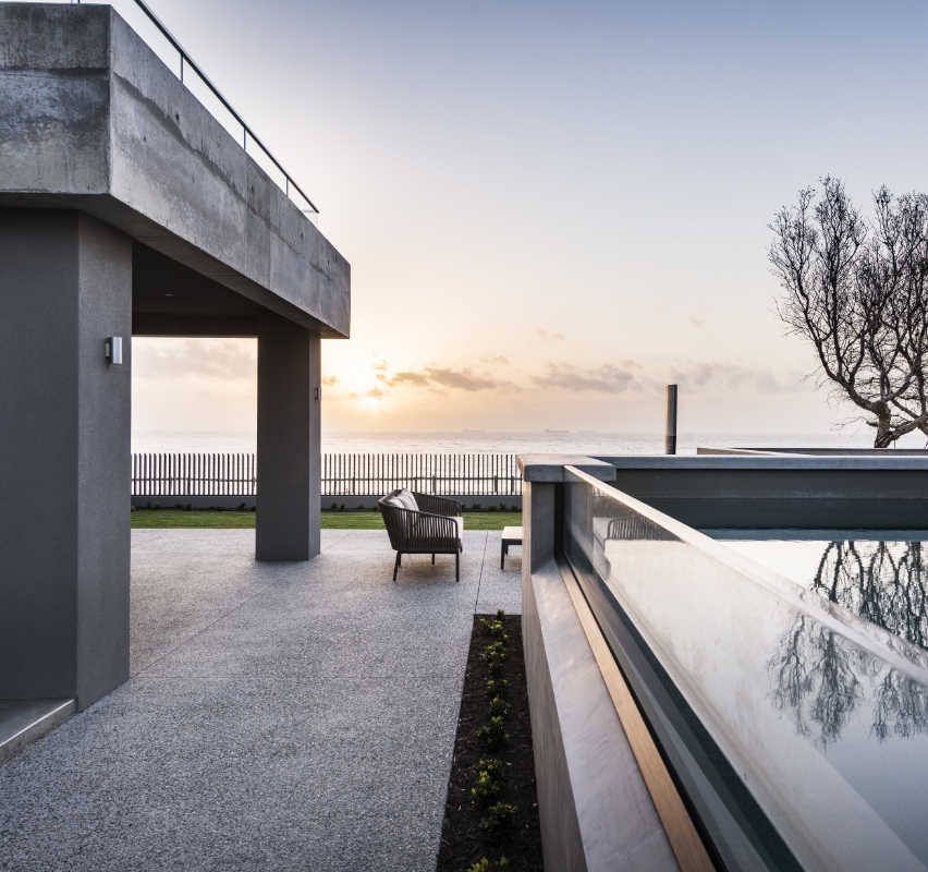 Modern seaside home at sunset with outdoor seating.